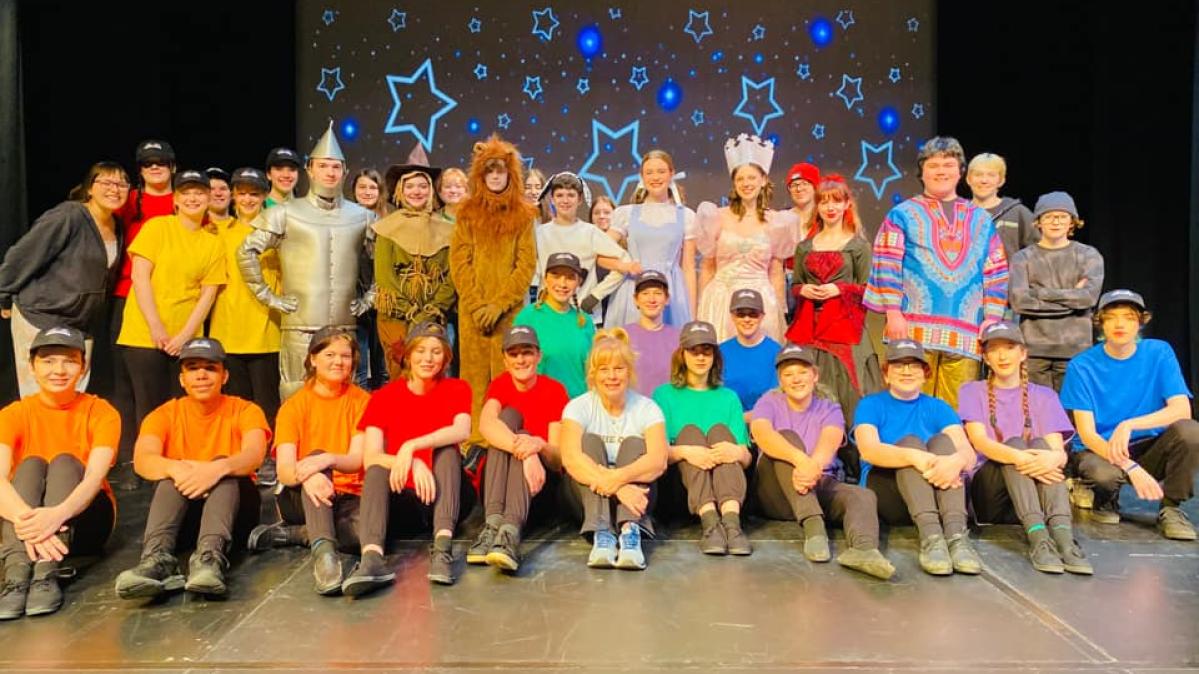 Students in colourful t-shirts sitting and standing as part of the cast of a school production of "OZ"